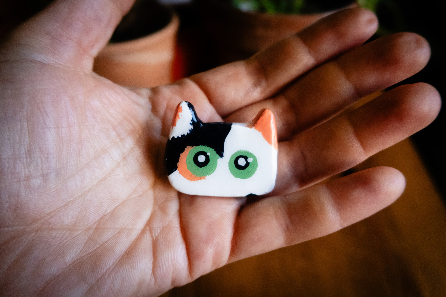 and holding a small tri-color cat-shaped polymer clay magnet