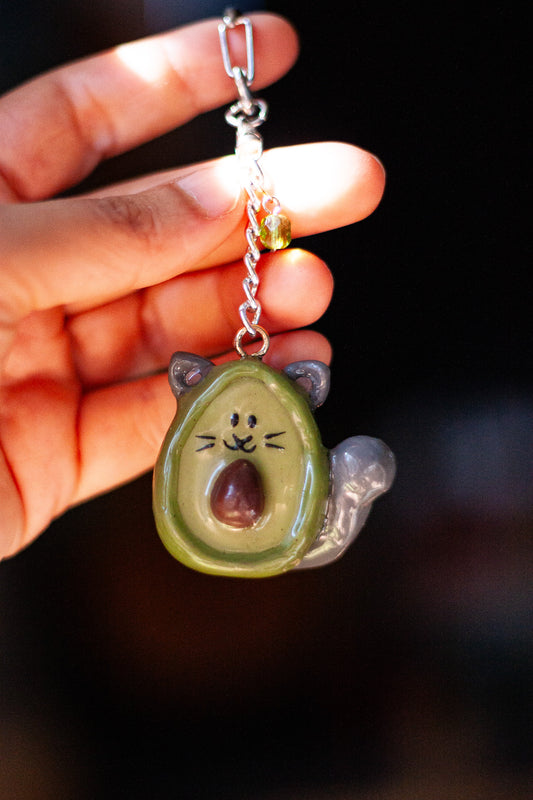 Avocado-shaped keychain with cat ears held by a hand against a dark background