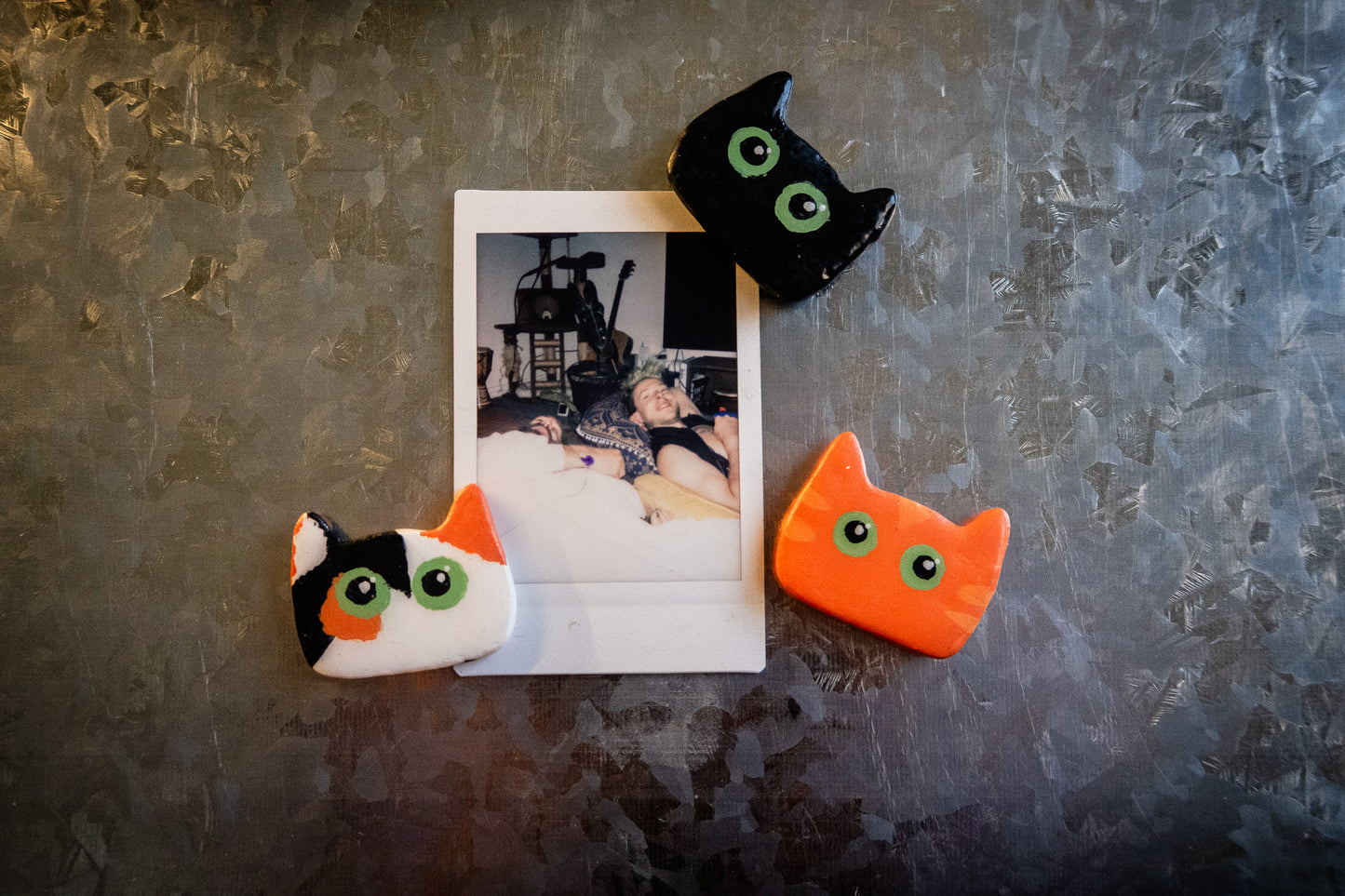 Three cat-shaped magnets on a textured surface with a small photo underneath.