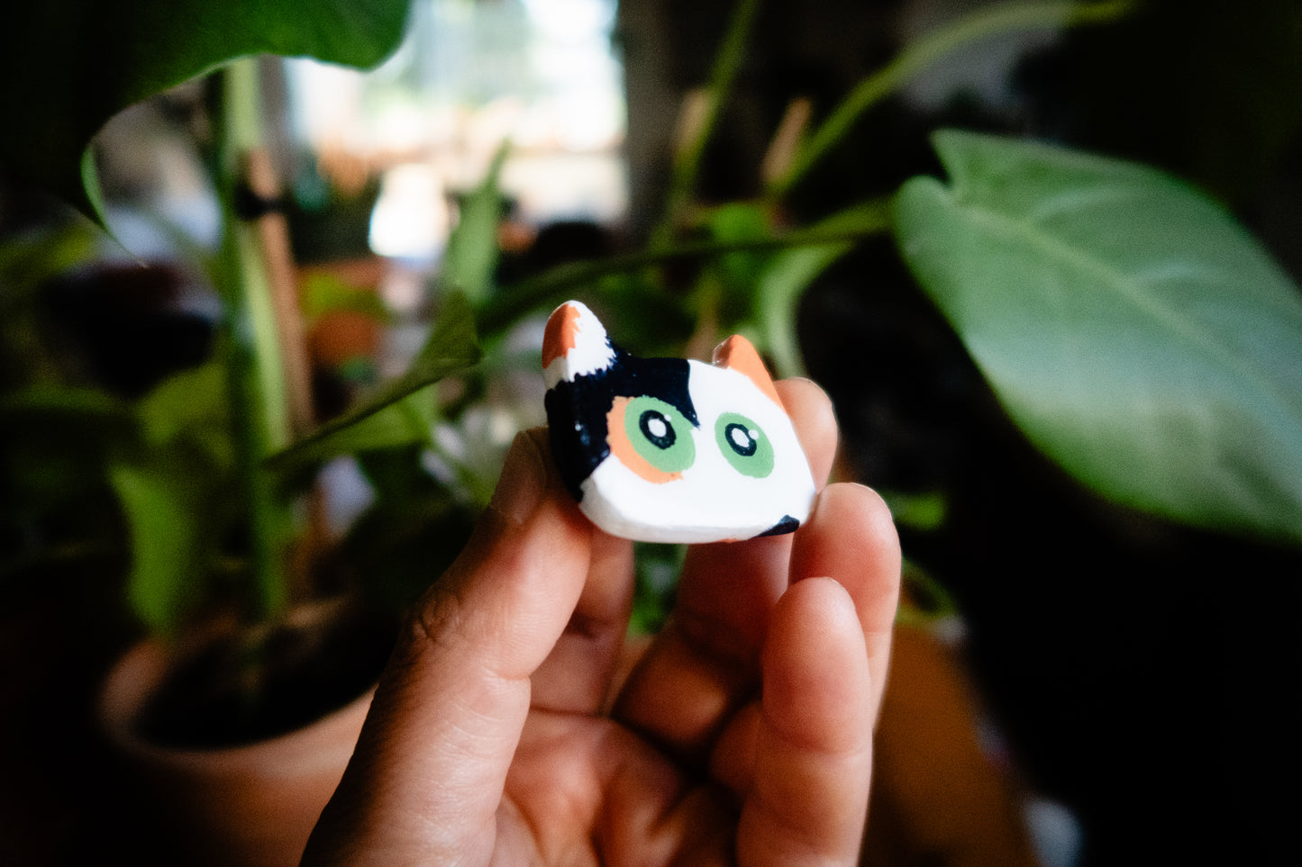 and holding a small tri-color cat-shaped polymer clay magnet with potted plants in the background